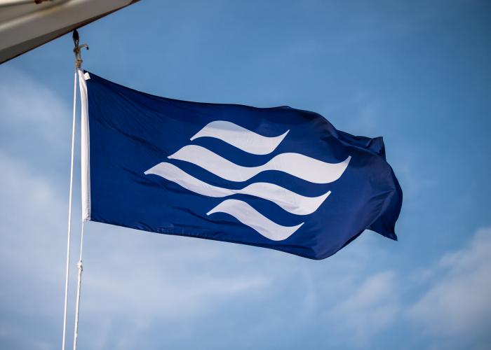 The royal blue Marine Atlantic flag with undulating white wave emblem blows in the wind onboard a ferry. 