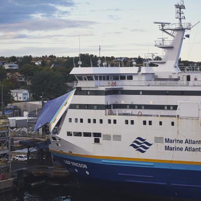 Vehicles prepare to board the open bridge of the Leif Ericson ferry, which is blue and white with a teal and yellow stripe. 
