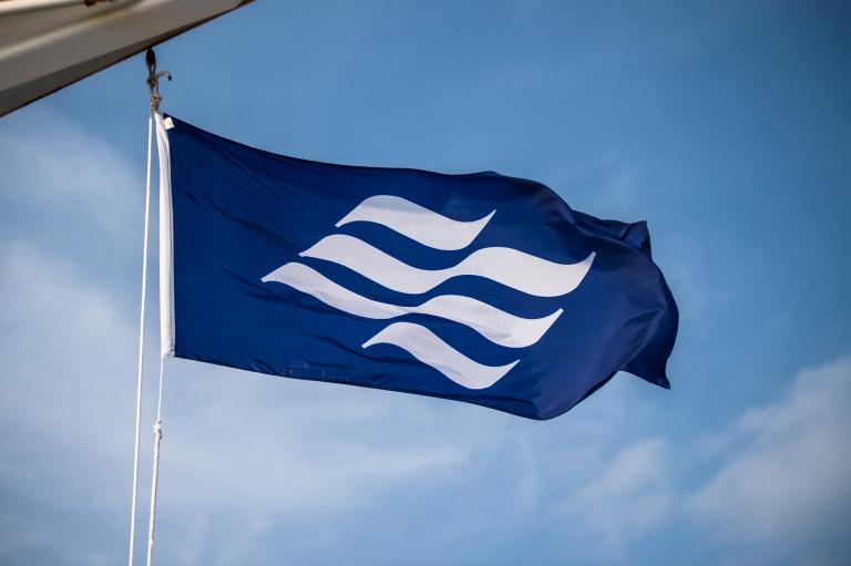 The royal blue Marine Atlantic flag with undulating white wave emblem blows in the wind onboard a ferry. 