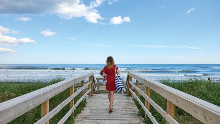 Woman waling onto beach from boardwalk.