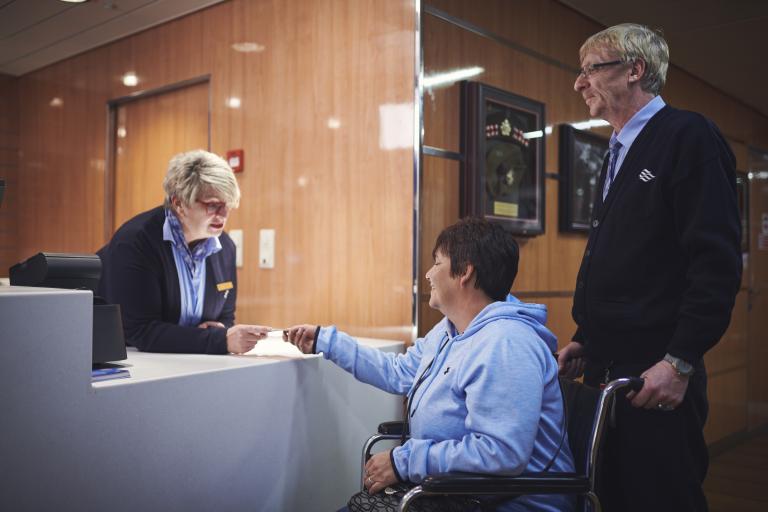 woman at desk handing card over to woman in wheelchair