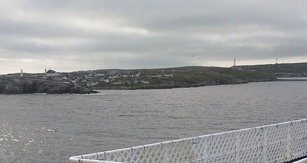 Image: view over rail of houses perched on rock as ship enters Port aux Basques harbour 