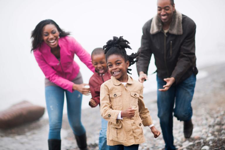 a family with two small children chase each other along the water