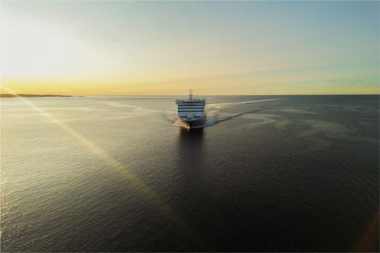 A large vessel crosses calm waters at sunrise