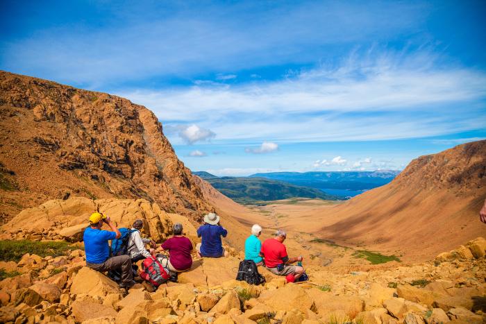 A group of six older hikers take a moment to rest and take in the scenery on the tablelands at Gros Morne National Park. 