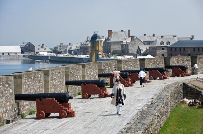 a person in traditional attire walks along bank of cannons pointed over water's edge through rock walls