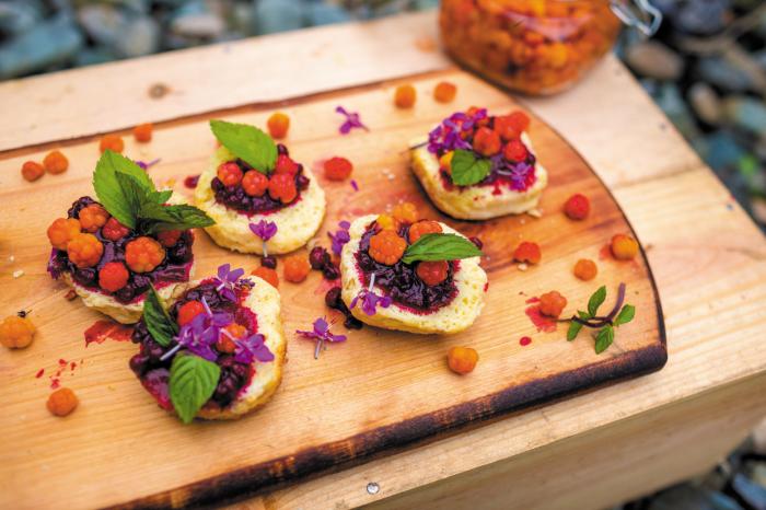 wooden board with five halved biscuits covered with berries and mint leaves
