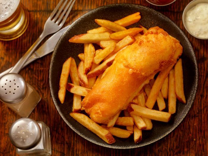 plate of deep fried fish and chips sit beside cutlery and salt & pepper shakers