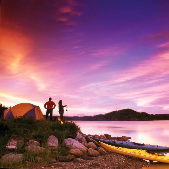 two people stand beside tent on edge of water during purple and red sky sunset
