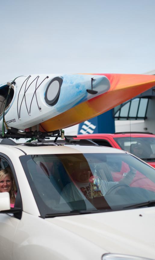 Passenger waving from car with kayaks on roof.